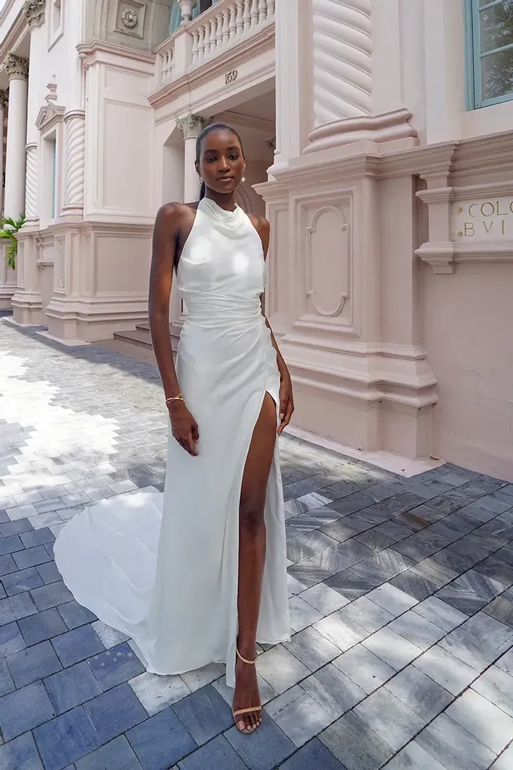 Woman in white dress with high slit stands outside a building.