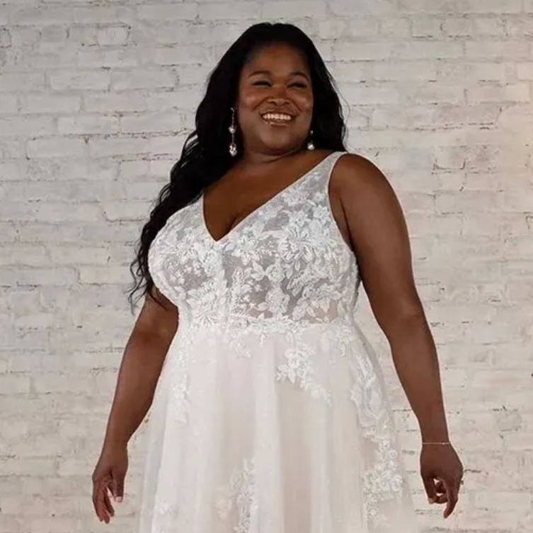 Woman in white wedding dress smiling in front of a white brick wall.