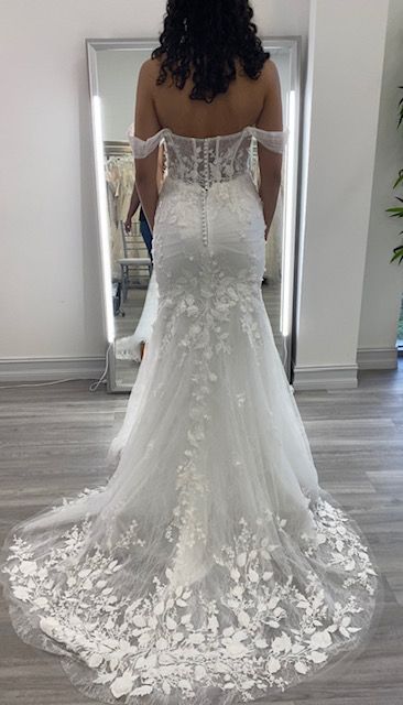 Woman in white dress with high slit stands outside a building.