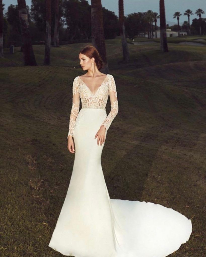Woman in a white wedding dress with a long train, standing on grass.