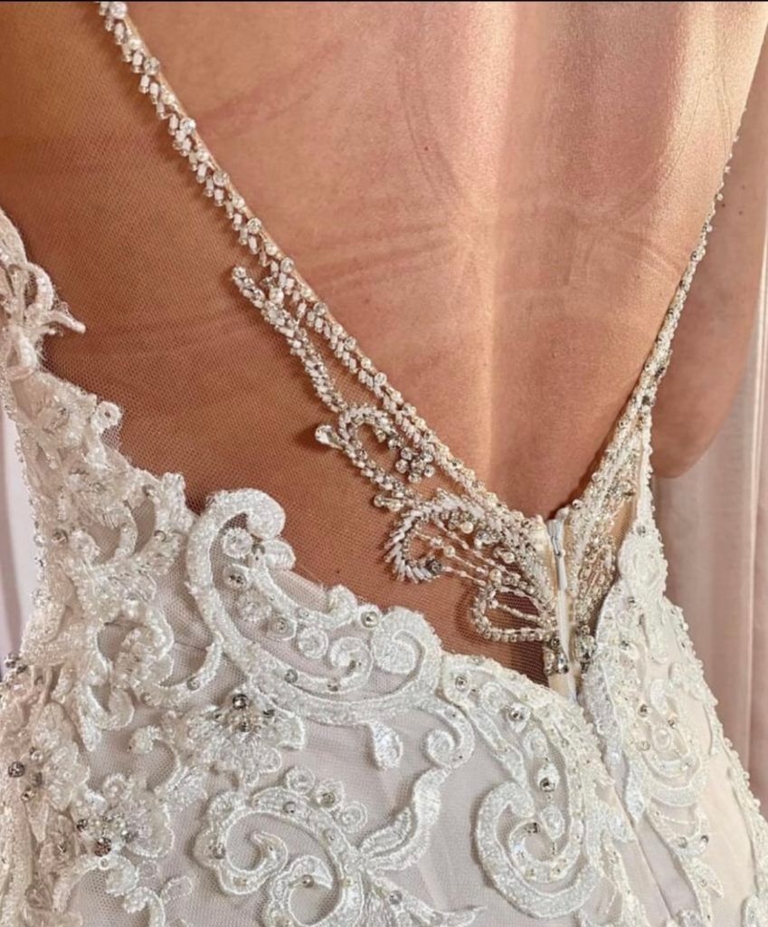 Close-up of a white wedding dress back with intricate lace and jeweled straps.