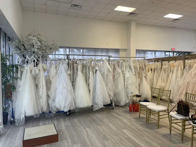 Wedding dresses on display in a bridal shop; racks of white gowns, chairs, and neutral setting.