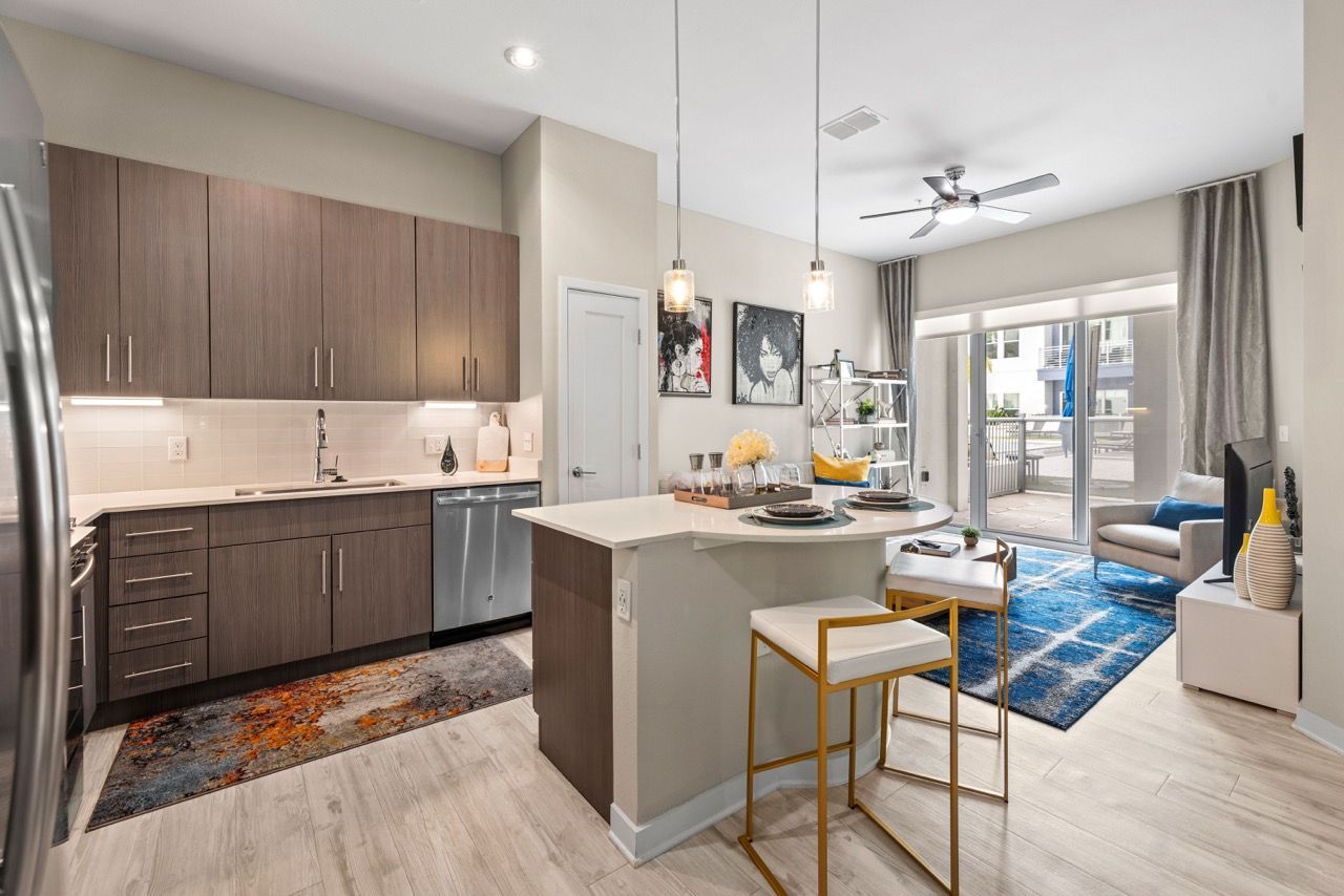 Open-concept apartment kitchen with island and living area, sliding glass door to balcony.