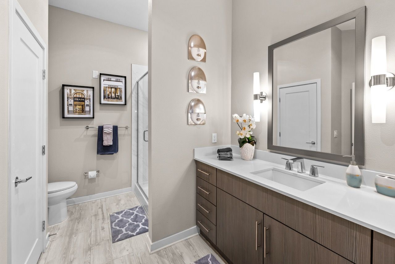 Modern bathroom with long vanity, large mirror, wall sconces, and glass shower.