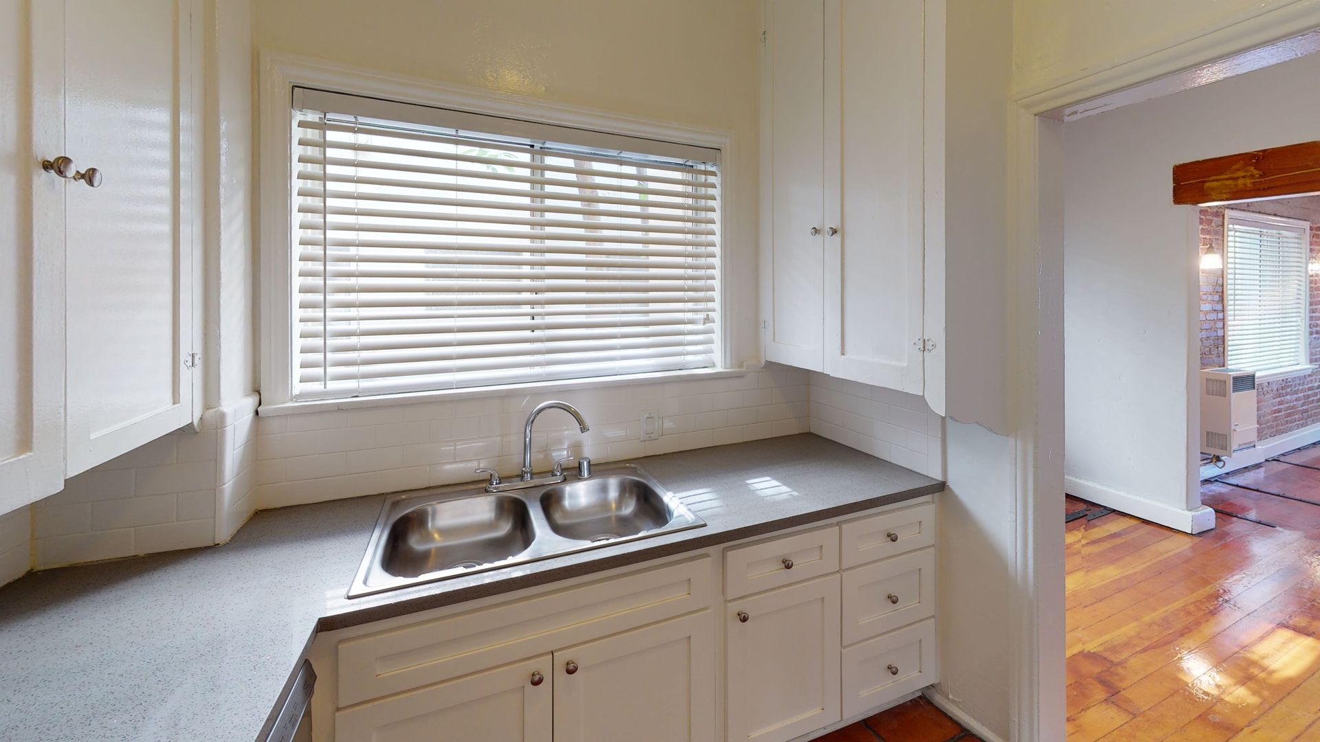 Kitchen with white cabinets, double sink, and a window with blinds.