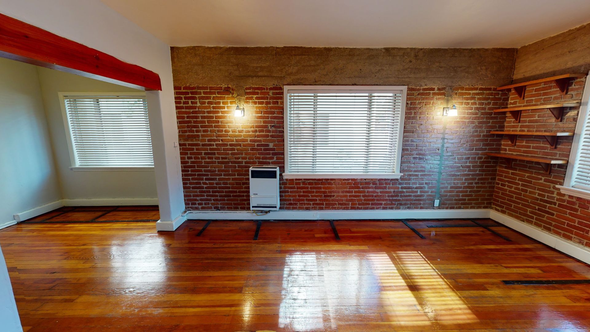 Empty room with brick accent walls, hardwood floors, and windows.
