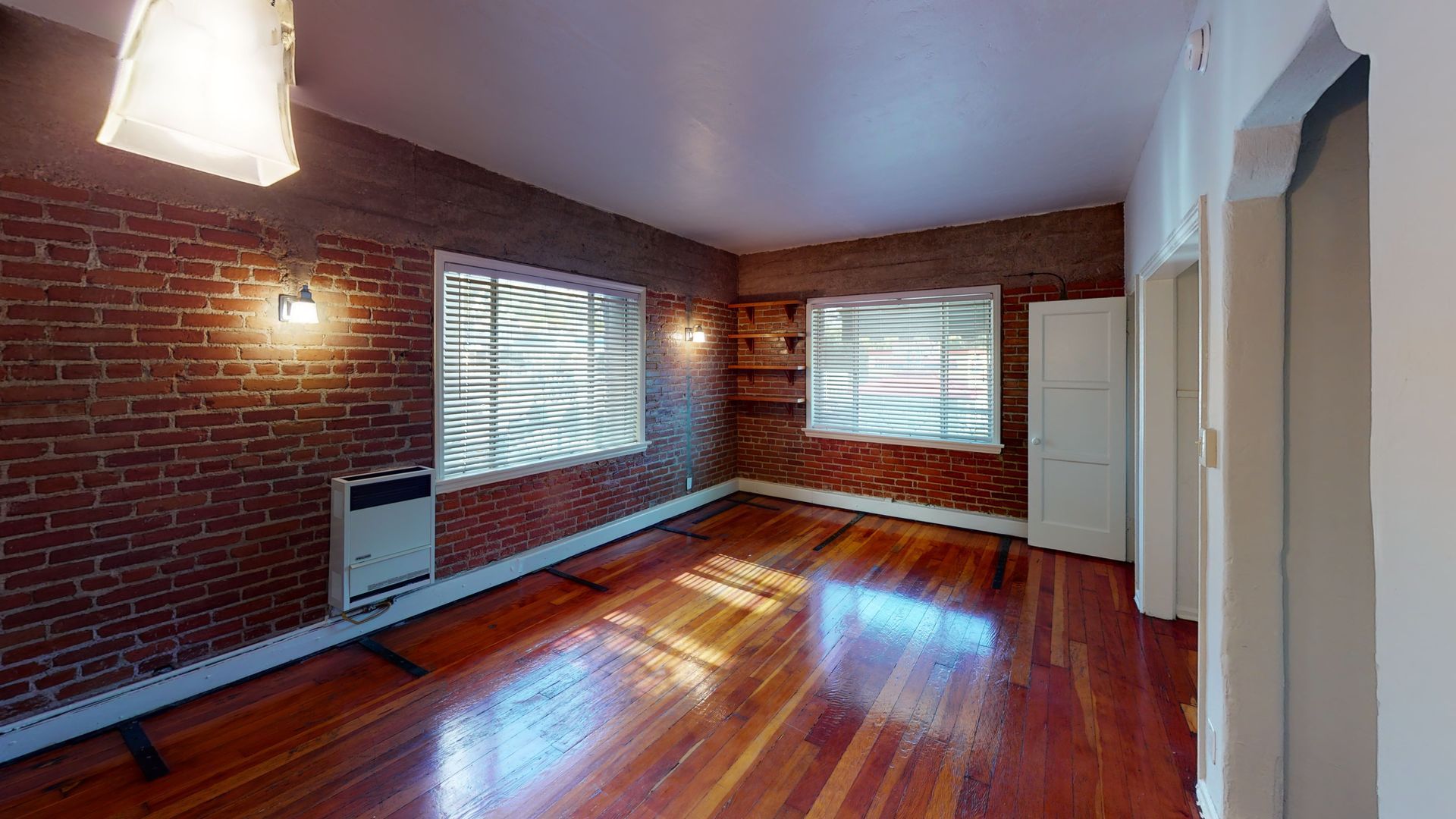 Brick-walled room with wooden floors, windows, and white cabinets.