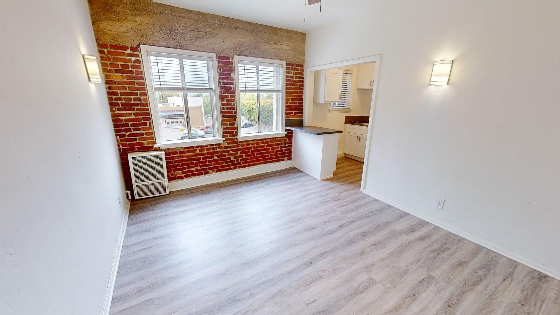 Empty apartment interior with brick accent wall and wood-look flooring.