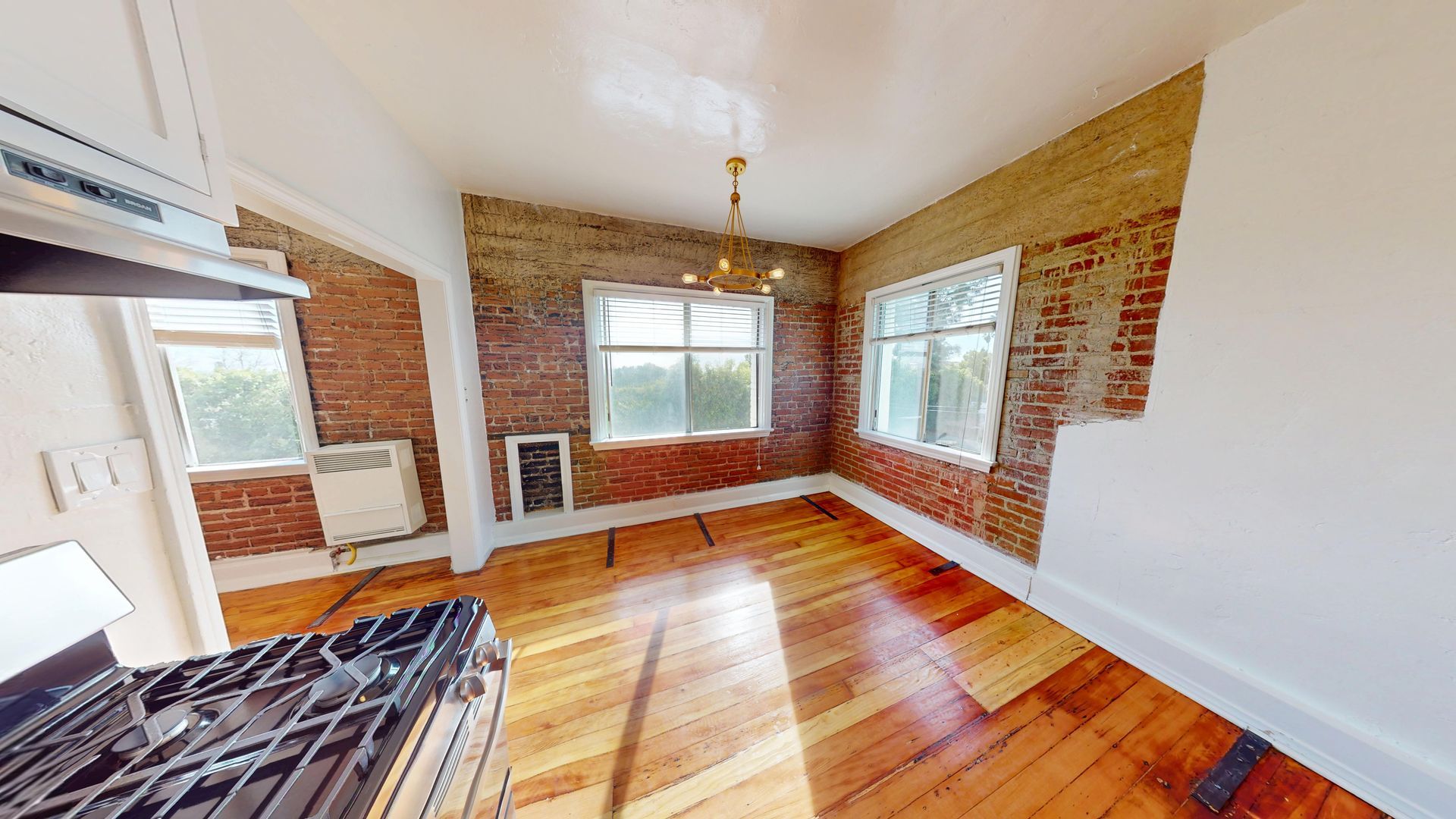 Interior of a room with brick walls, hardwood floors, and windows. A gas stove is visible in the foreground.
