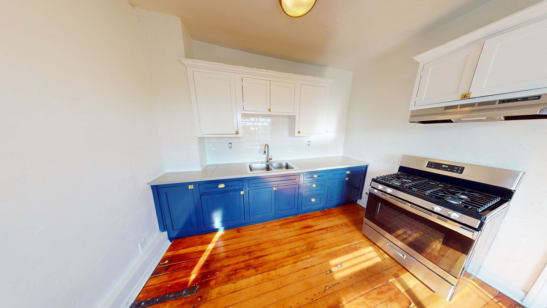 Kitchen with blue cabinets, white upper cabinets, and a stainless steel stove on a hardwood floor.