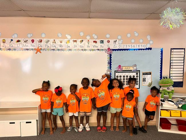 A group of children wearing orange shirts are standing in a classroom.