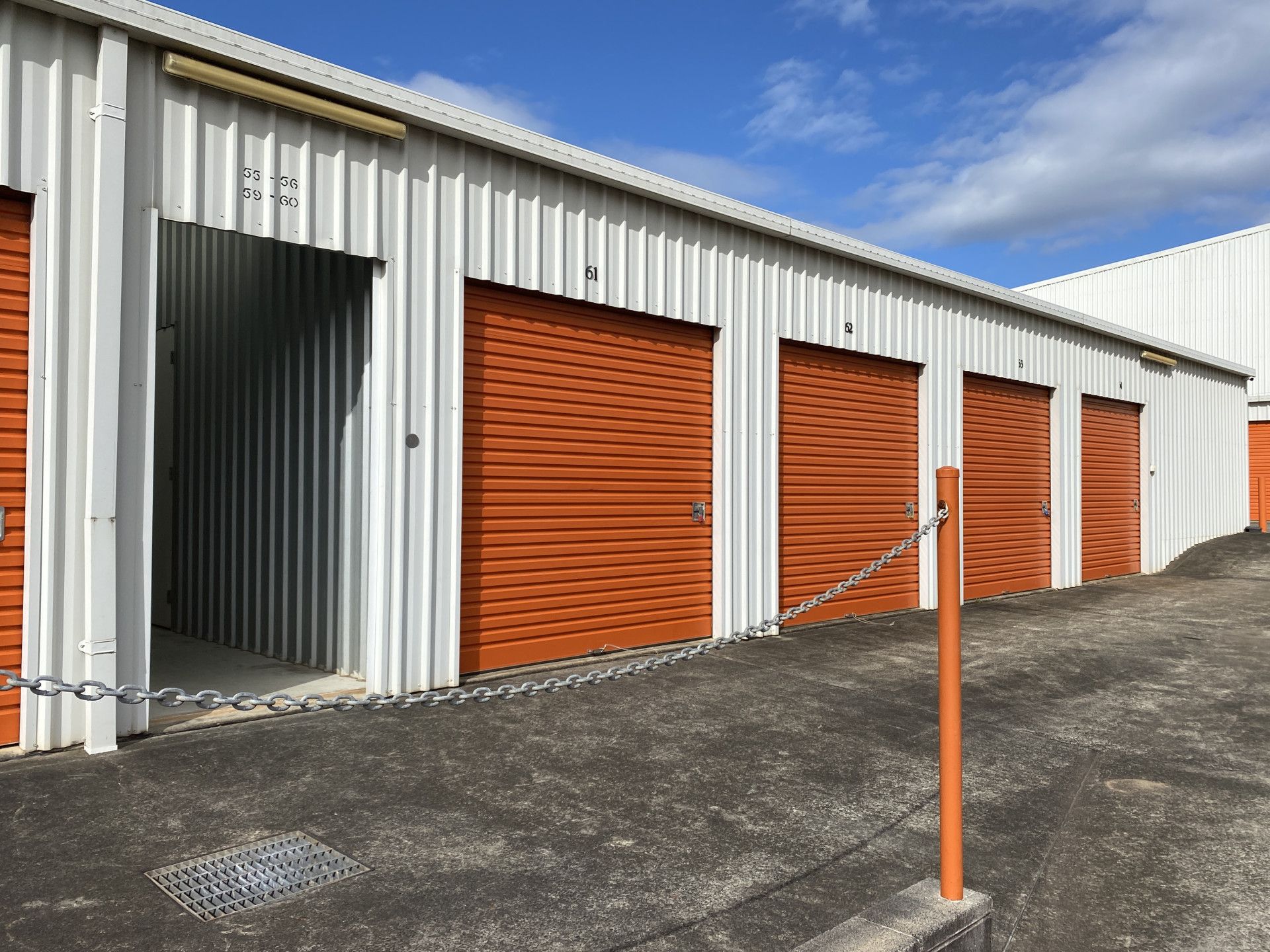 A row of storage units with orange doors and a chain link fence. — Acacia Mini Storage in Port Macquarie, NSW