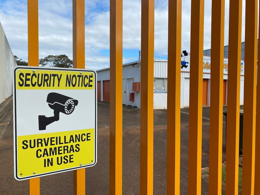 An orange Fence With A Yellow Security Notice That Says Surveillance Cameras In Use  — Acacia Mini Storage in Port Macquarie, NSW