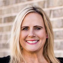 a woman with blonde hair is smiling in front of a brick wall