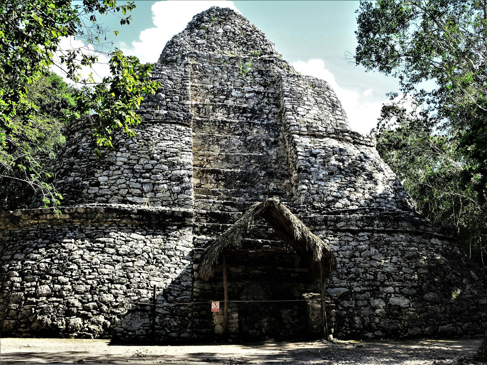 Un gran edificio de piedra con techo de paja está rodeado de árboles