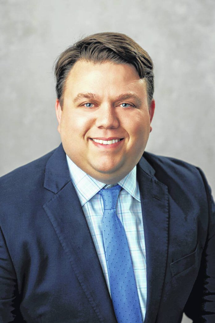 Man in a blue suit smiles at the camera, wearing a patterned blue tie.
