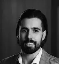 Um homem com barba está vestindo um terno e sorrindo em uma foto em preto e branco.