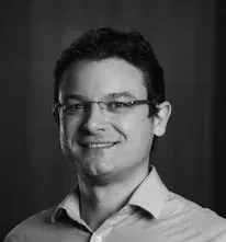 Um homem usando óculos e uma camisa branca está sorrindo em uma foto em preto e branco.