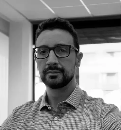 Um homem usando óculos e uma camisa branca está sorrindo em uma foto em preto e branco.