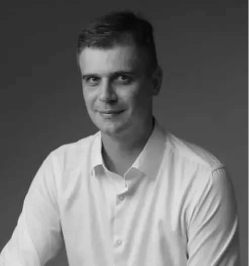 Um homem de terno e camisa branca está sorrindo em uma foto em preto e branco.