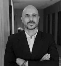 Um homem careca com barba está vestindo um terno e está de pé com os braços cruzados.