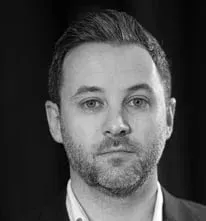 Um homem com barba e terno está olhando para a câmera em uma foto em preto e branco.