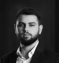 Um homem com barba está vestindo um terno e uma camisa branca.