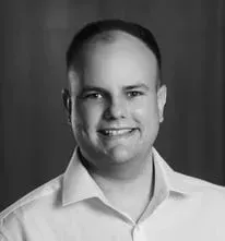 Um homem de camisa branca está sorrindo em uma foto em preto e branco.