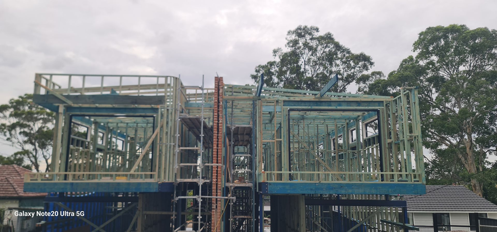 Construction site showing the timber frame and upper-level structure of a two-story building under a cloudy sky.