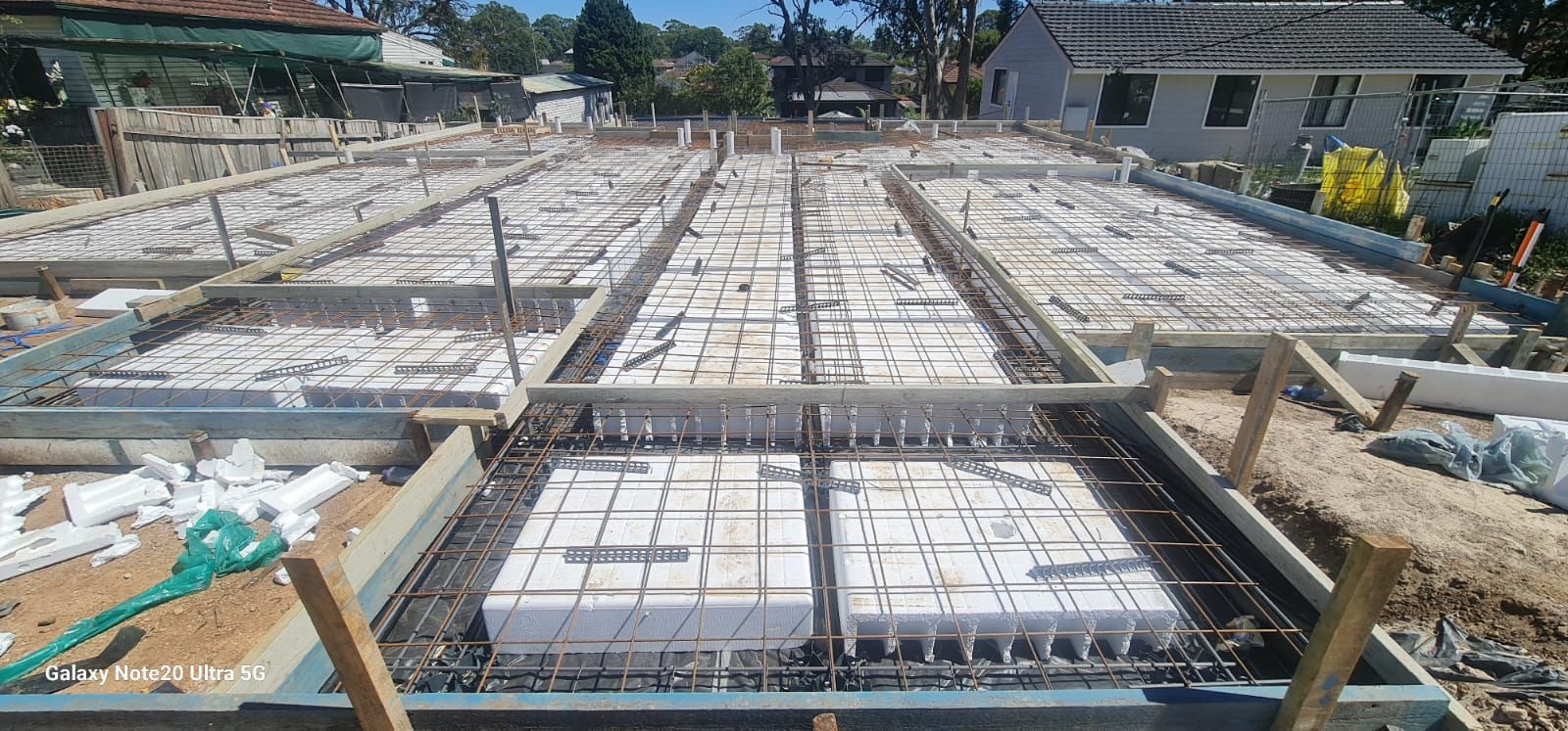 A construction site showing a waffle pod slab foundation with white polystyrene blocks arranged in a grid with steel mesh.