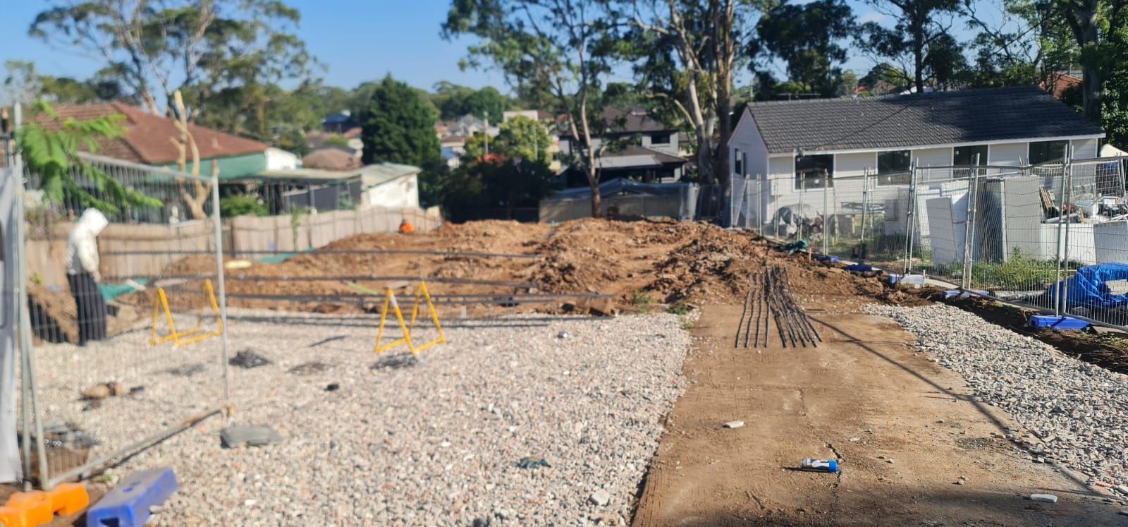 A construction site with gravel, piles of dirt, and metal reinforcement bars being prepared for a building foundation.