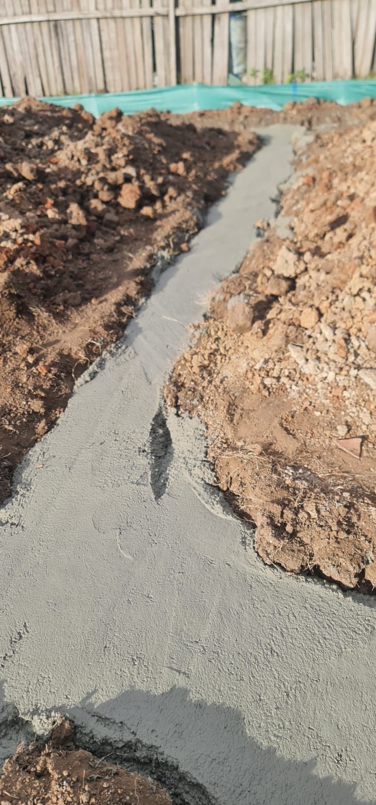 A freshly poured concrete foundation strip set in a dirt trench outdoors, viewed from above.