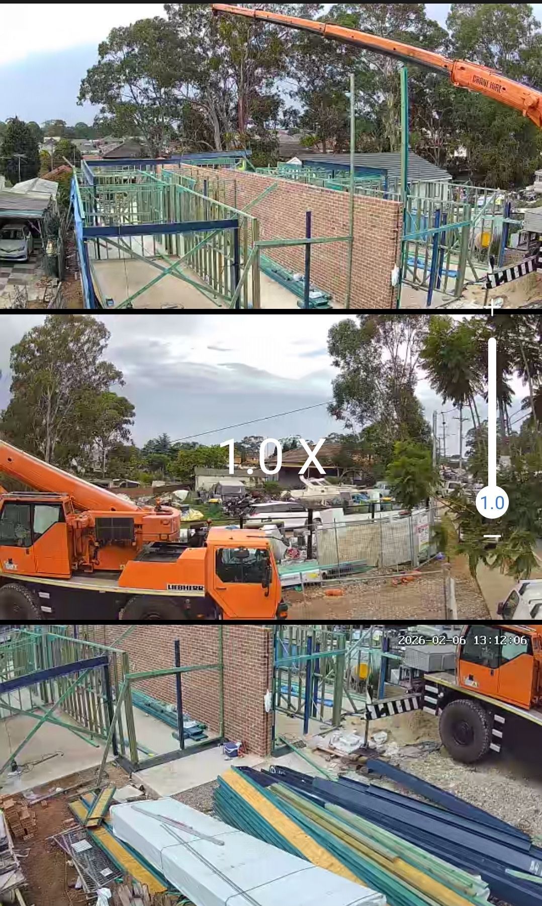 A construction site with an orange mobile crane, wooden framing, brick walls, and stacked metal beams.