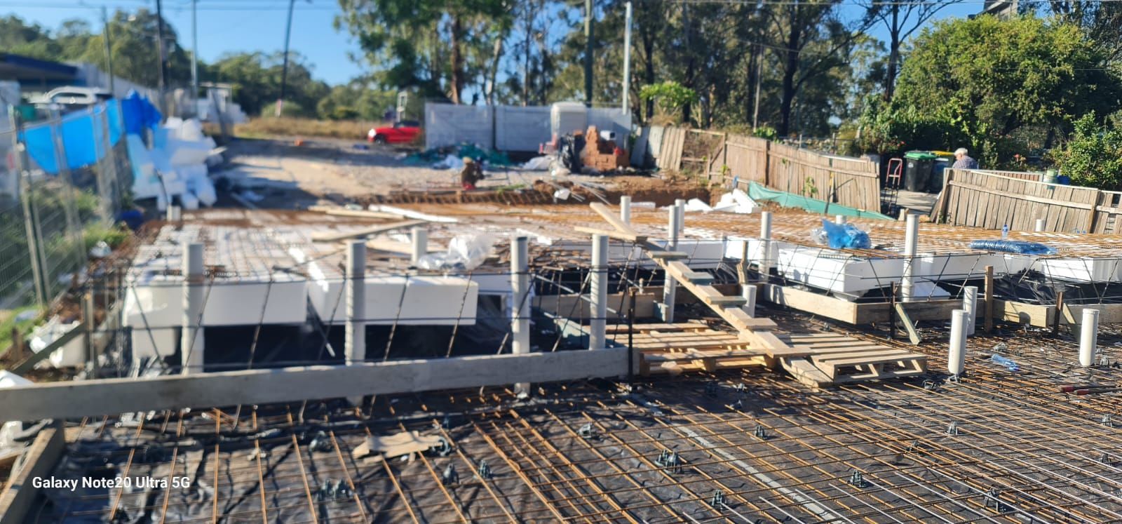 Construction site showing a prepared concrete slab foundation with white blocks and reinforcement bars ready for pouring.