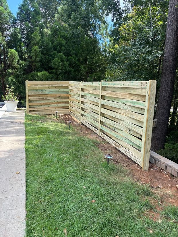 Wooden horizontal slat fence in a yard with green grass and trees.