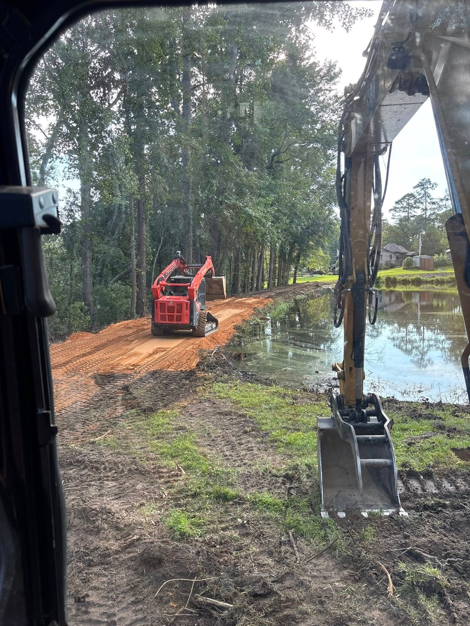 A construction scene with a red skid steer, excavator, and pond, clearing land near a tree line.