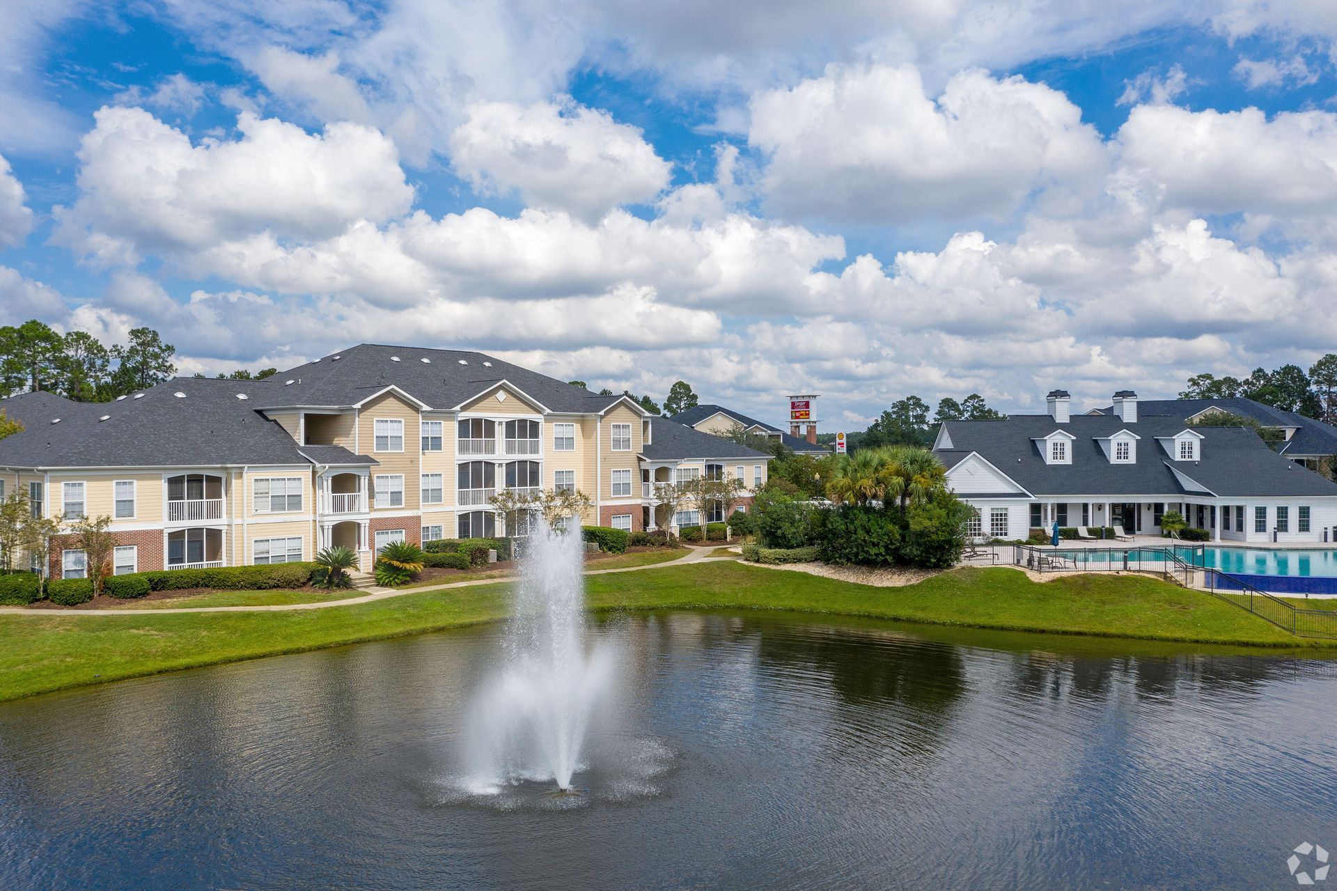 Apartment complex with fountain in lake, blue sky, and a pool at Preserve at Godley Station in Pooler, GA.