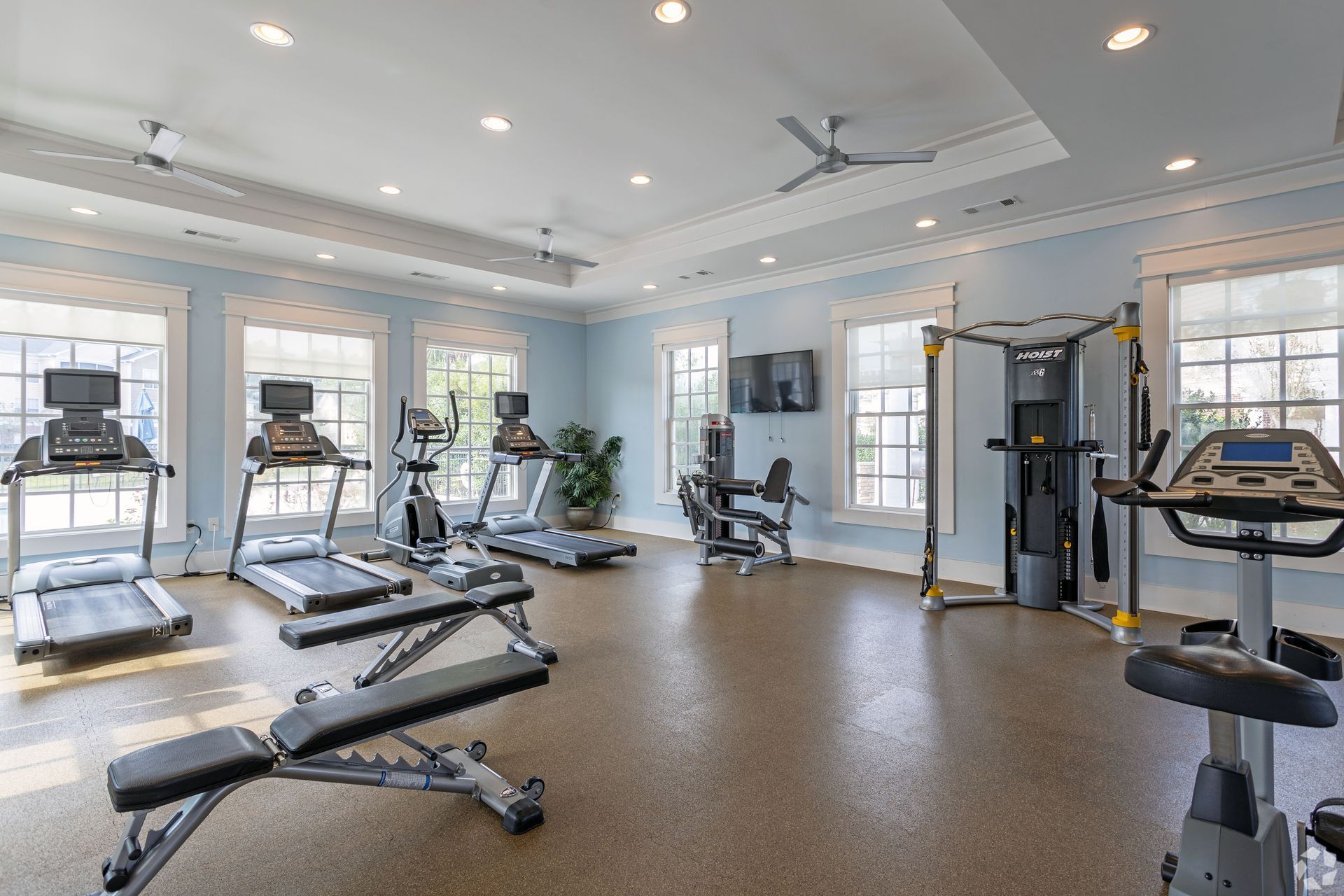 Gym interior with treadmills, weight bench, exercise machines, and windows at Preserve at Godley Station in Pooler, GA.