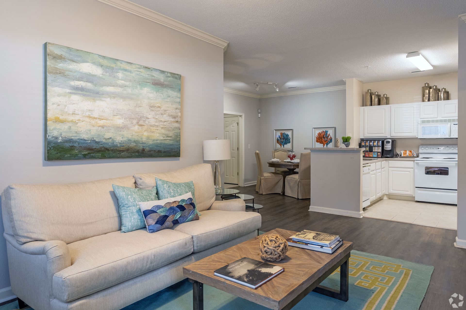 Living room with white sofa, blue and gold artwork, open to a kitchen with white cabinets at Preserve at Godley Station in Pooler, GA.