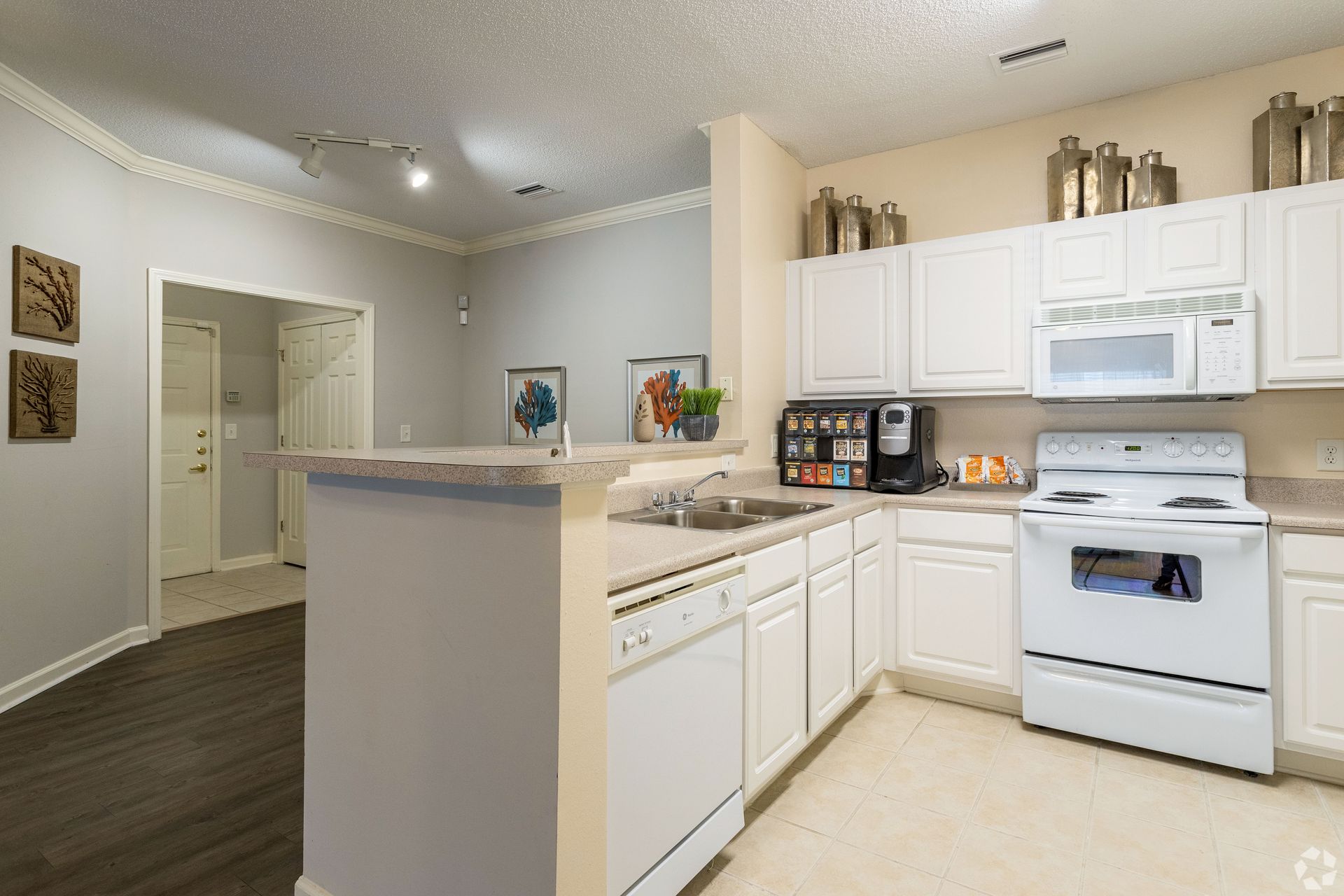 White kitchen with white appliances, cabinets, and light countertops; tan walls and tile floor at Preserve at Godley Station in Pooler, GA.
