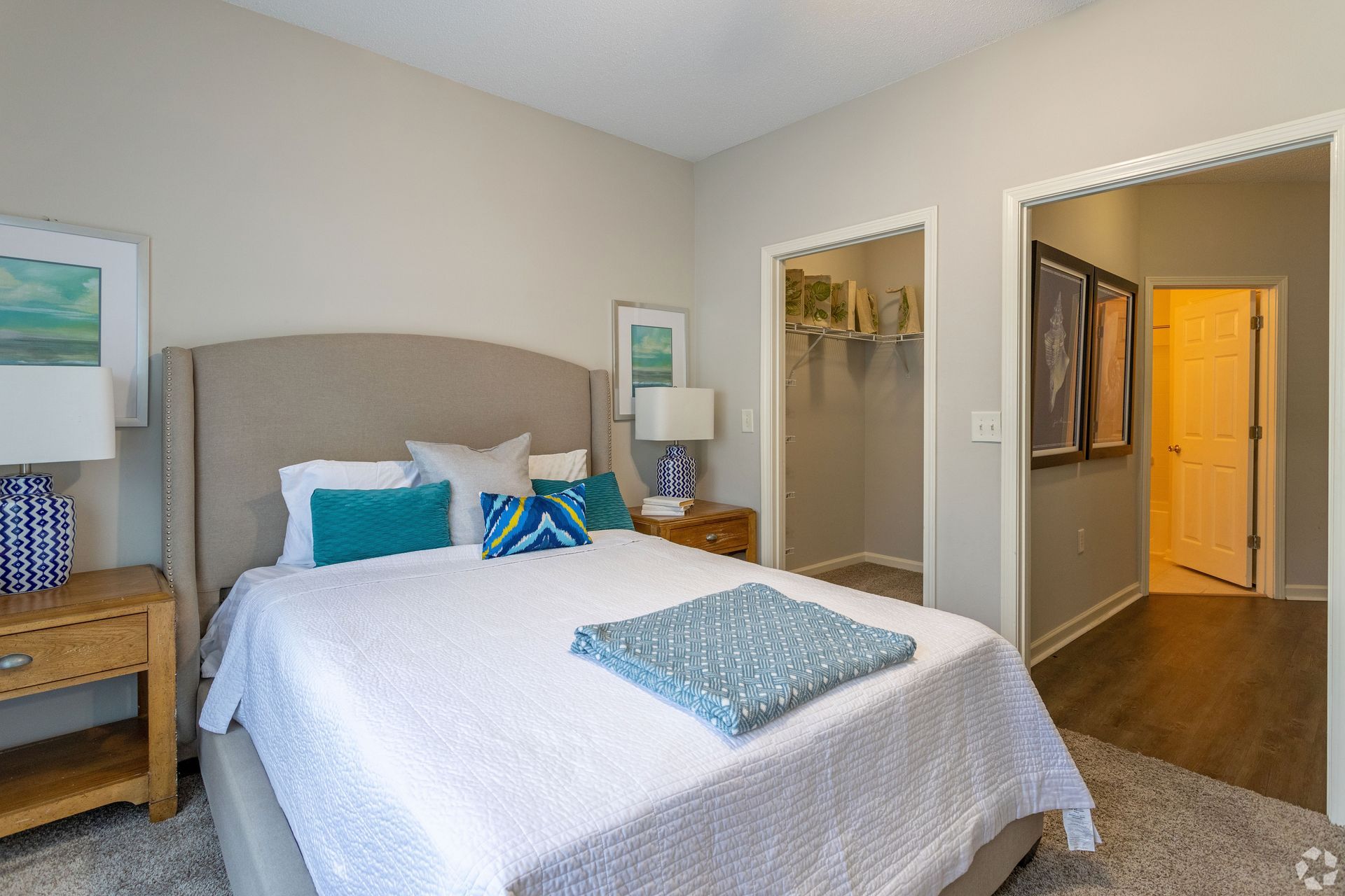 Bedroom with bed, nightstands, closet, and neutral-toned walls. Teal and blue accents, wooden floors at Preserve at Godley Station in Pooler, GA.