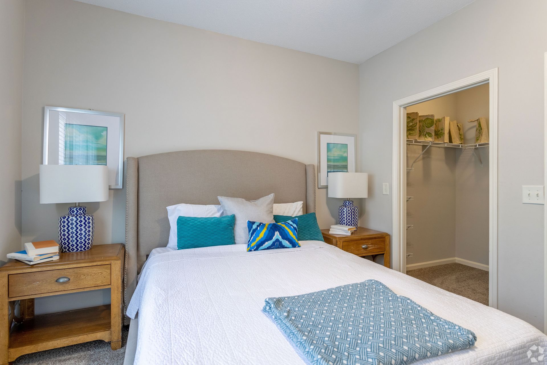 Bedroom with bed, nightstands, lamps, and closet. Teal and white decor, neutral walls at Preserve at Godley Station in Pooler, GA.