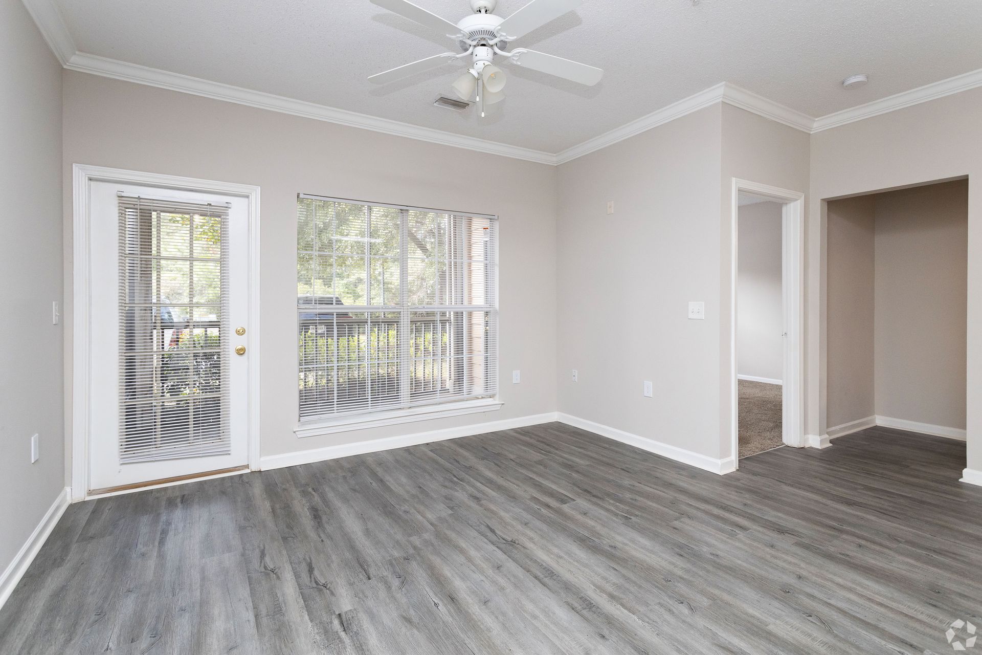 Empty room with gray wood-look flooring, light walls, and a door and window looking out to a balcony at Preserve at Godley Station in Pooler, GA.