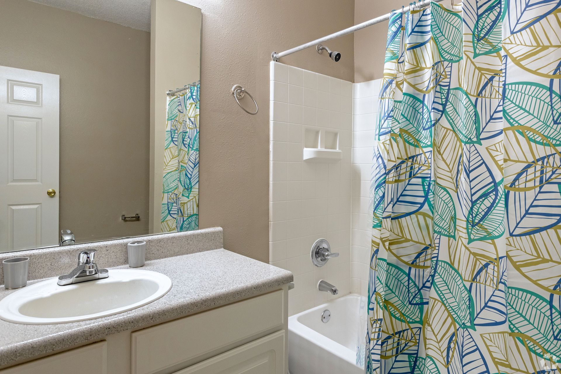Bathroom with a white sink, tub, and walls, featuring a leaf-patterned shower curtain at Preserve at Godley Station in Pooler, GA.