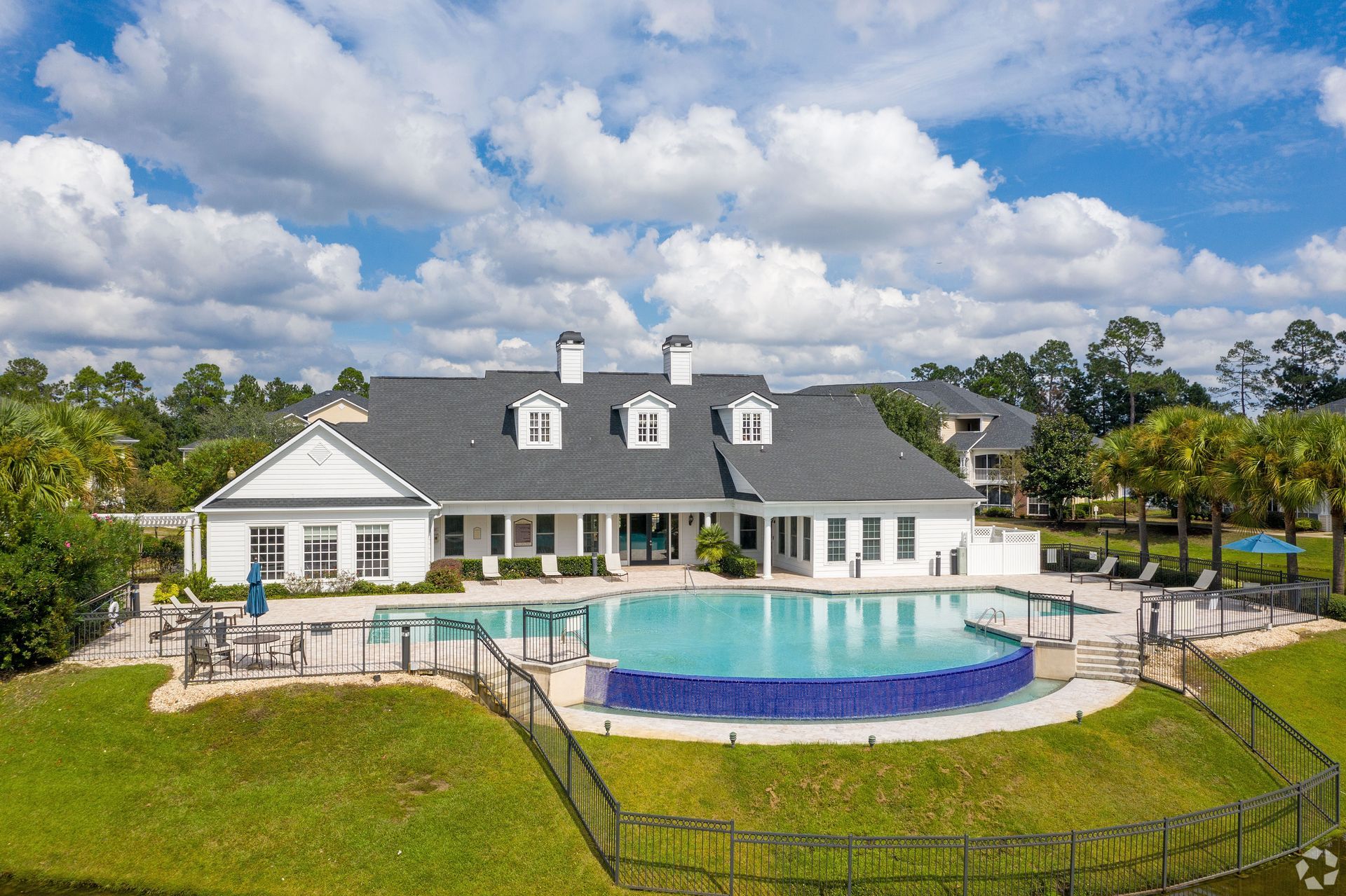 Pool and clubhouse at an apartment complex under a blue sky with fluffy clouds at Preserve at Godley Station in Pooler, GA.