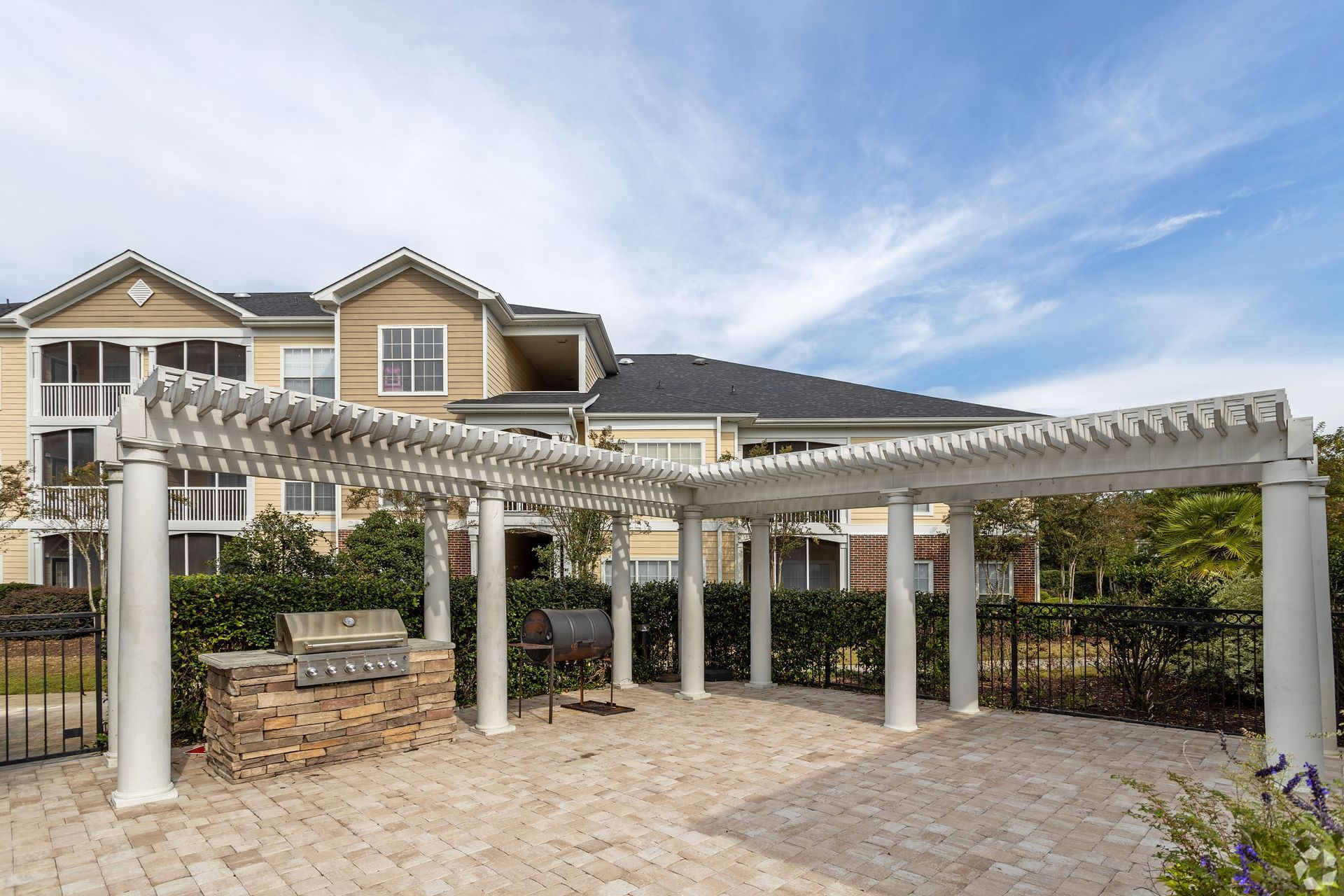 Outdoor patio with a white pergola, brick grill, and apartment building in the background at Preserve at Godley Station in Pooler, GA.