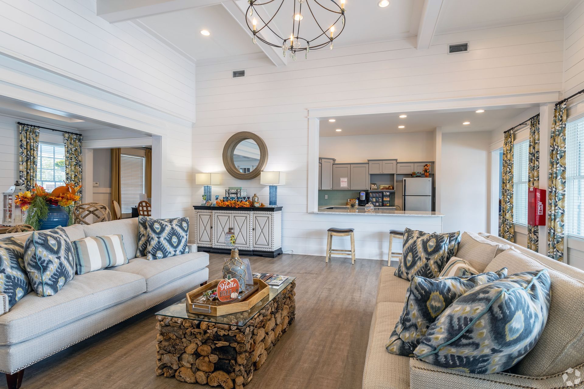 Spacious living room with sofas, a rustic coffee table, and an open kitchen area. Neutral tones with blue accents at Preserve at Godley Station in Pooler, GA.