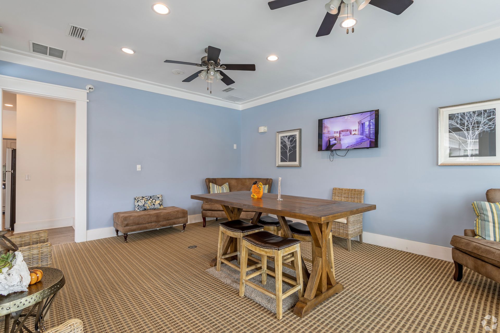 Cozy living room with blue walls, a large wooden table, brown seating, and a mounted TV at Preserve at Godley Station in Pooler, GA.