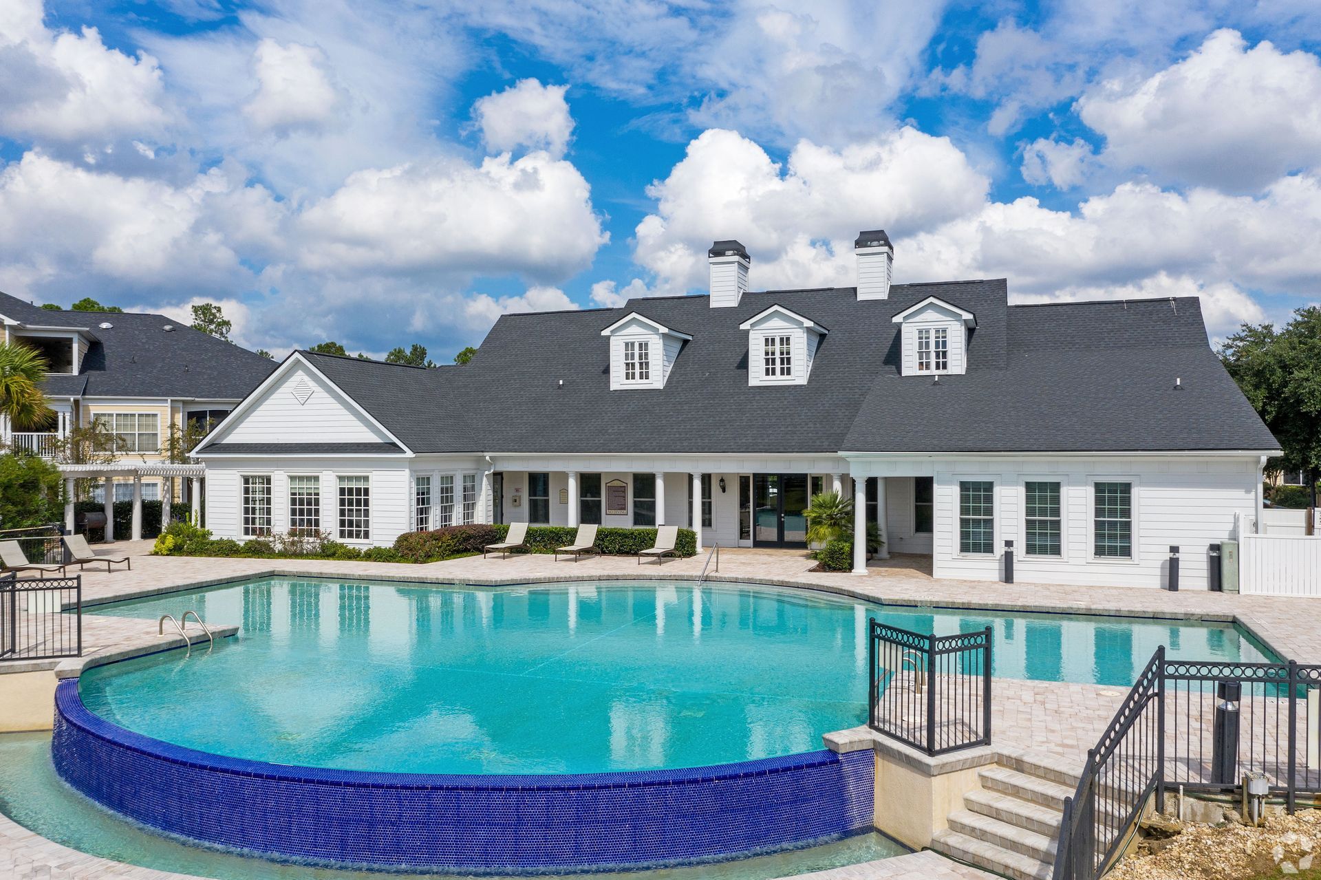 Pool and white building with dark roof, three dormers, blue water, sunny day at Preserve at Godley Station in Pooler, GA.