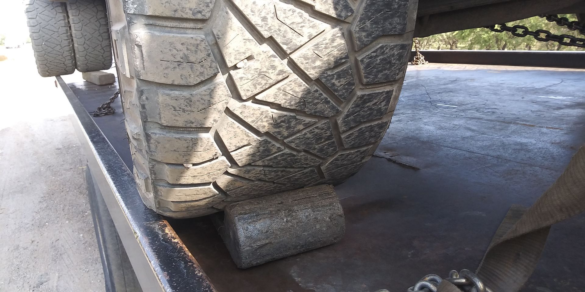 A truck tire on a flatbed trailer is resting on a wheel chock to prevent rolling during transport.